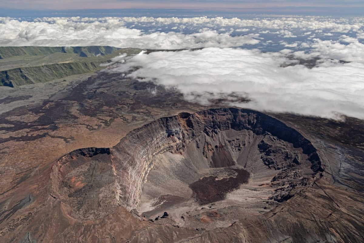 Vue aérienne du cratère Dolomieu du Piton de la Fournaise à La Réunion : caldeira béante au-dessus de la mer de nuages, paysage volcanique brut, illustration du volet Réunion du combiné